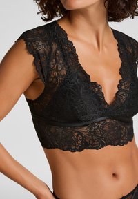 Schwarzer Spitzen-Bralette mit kurzen Ärmeln, tiefem V-Ausschnitt, floralen Mustern und einem satinierte Bündchen am unteren Saum. Strukturierte und zarte Gestaltung.