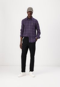 Purple plaid shirt with button front, yellow logo, black pants, and white sneakers. Hat is gray with embroidered text.