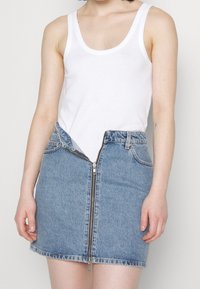 Jeanskjol med framdragkedja och fickor, med en klassisk blåtvätt. Matchad med en vit ärmlös topp. Enkel design, avslappnad stil.