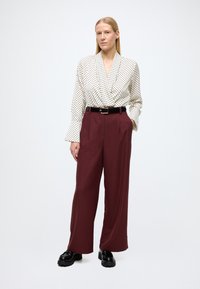 Bijela i crna bluza s točkicama i širokim rukavima, uparena s bordo visokim hlačama i crnim masivnim cipelama.