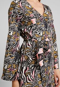 Sukienka wrap w kolorze czarnym, z odważnym abstrakcyjnym wzorem w różowe, złote i białe akcenty. Długie rękawy i detal w postaci wiązania w talii.