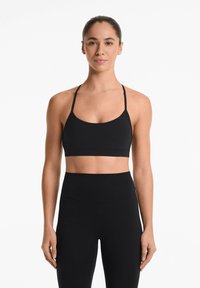Zwarte sportbeha met dunne bandjes, een ronde halslijn en een gladde textuur, gecombineerd met hoge zwarte leggings.