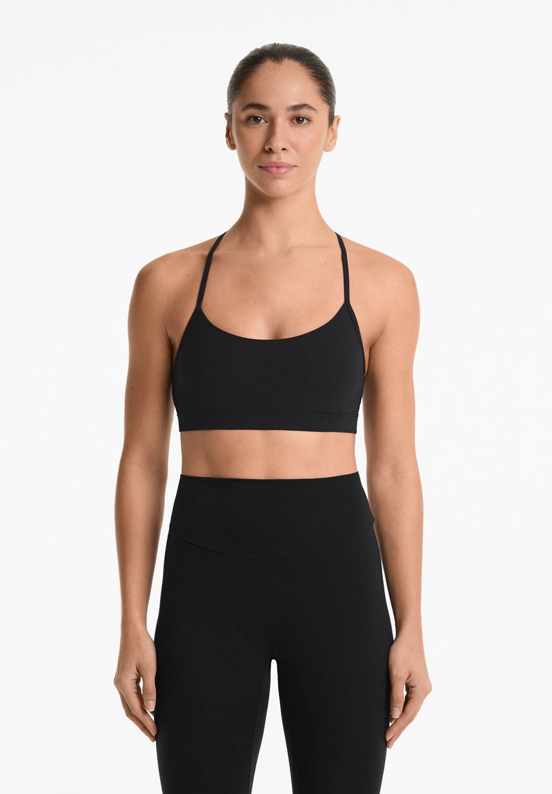 Zwarte sportbeha met dunne bandjes, een ronde halslijn en een gladde textuur, gecombineerd met hoge zwarte leggings.