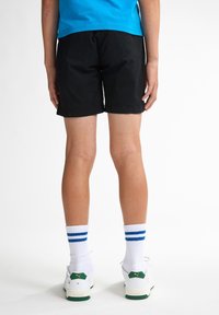 Pantalones cortos negros, de tela suave, hasta la rodilla. Calcetines blancos con rayas azules, usados con zapatillas blancas con acentos verdes.