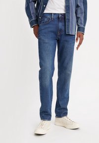 Blå denimjeans med rak passform, klassisk femficksdesign och lätt slitning. Kombineras med vita sneakers och en randig skjorta.