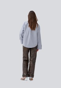 Stribet blå og hvid oversized skjorte, parret med mørkebrun læderbukser og lyseblå højhælede sandaler, set bagfra.