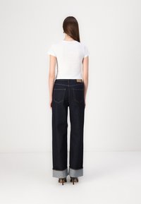 Jeans anchos de mezclilla azul oscura con puños doblados y un parche de cuero en la cintura. Combinados con una blusa ajustada de manga corta blanca.