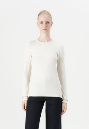 Lange mouwen crème ribbel top, ronde halslijn, zachte textuur, aansluitende silhouet, gecombineerd met donkere wijde jeans.