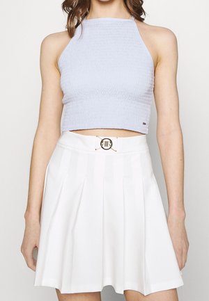 Lichtblauw gerimpeld cropped topje gecombineerd met een witte geplooide rok met een gouden gespaccent bij de taille.