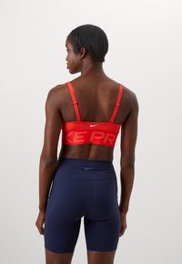 Red sports bra with a bold "NIKE PRO" print and adjustable straps, paired with navy blue high-waisted shorts. Smooth, stretchy fabric.