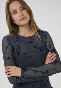 Langsleeve top in donkergrijs met doorschijnend bloemenpatroon. Gestructureerde stof met een fitted ontwerp en ronde halslijn. Details op de mouwen en zoom.