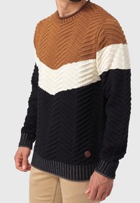 Pull en maille avec motif chevron en marron, crème et noir. Tissu texturé avec poignets et ourlet côtelés. Accent de logo discret.