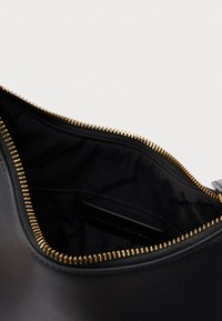 Fekete bőr táska arany színű cipzárral, részben nyitva, fekete vászon bélés látható, amelyen a "KARL LAGERFELD" felirat szerepel.