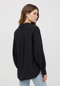 Camicia nera a maniche lunghe con colletto, vestibilità rilassata e polsini con bottoni. Realizzata in tessuto morbido, presenta dettagli con pieghe sul retro.