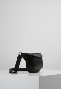 Riñonera de cuero negro con diseño curvo, cierre superior con cremallera y correa de tela ajustable. Textura lisa con detalles metálicos plateados.