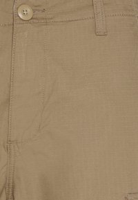 Tissu beige avec un motif à carreaux subtil, doté d'une fermeture à bouton et de détails de couture visibles. Une texture lisse avec un léger éclat.
