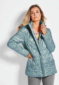 Türkise isolierte Jacke mit einem gesteppten Muster, Stehkragen und Druckknöpfen; verfügt über Fronttaschen und eine glatte, glänzende Oberfläche.