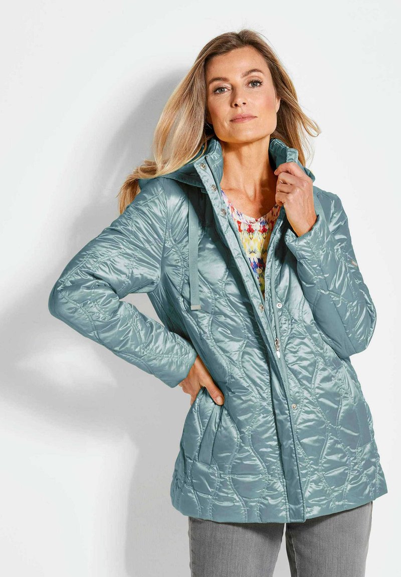 Türkise isolierte Jacke mit einem gesteppten Muster, Stehkragen und Druckknöpfen; verfügt über Fronttaschen und eine glatte, glänzende Oberfläche.