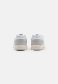 White leather sneakers with gray suede accents, featuring a textured rear panel and a beige rubber sole. Logo embossed on heel.