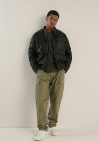 Czarna kurtka bomber z sztucznej skóry z prążkowanymi ramionami, oliwkowe spodnie cargo i białe sneakersy. Gładkie kolory, casualowy design, funkcjonalne kieszenie.