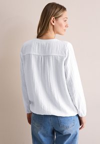 Witte getextureerde blouse met lange mouwen en een ronde halslijn, met een yoke-detail op de rug, gecombineerd met lichtblauwe denim jeans.