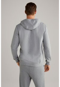 Sudadera gris con capucha, que cuenta con una tela texturizada, puños y cintura elásticos. La vista trasera muestra el diseño ajustado y las costuras.