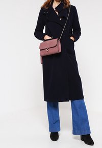 Długi granatowy płaszcz o podwójnym zapięciu, z teksturowanej tkaniny i bocznymi kieszeniami. Zestawiony z dżinsami o szerokich nogawkach i różową torebką na ramię.