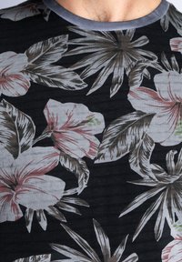 Camiseta de manga corta negra con diseño floral gris que presenta flores rosas y acentos verdes, terminada con un cuello redondo ribeteado en gris.