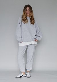 Szary sweatshirt i dresy z białą koszulką pod spodem, o luźnym kroju i ściągaczach przy mankietach. Połączone z trampkami w czarne paski.