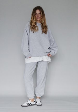 Szary sweatshirt i dresy z białą koszulką pod spodem, o luźnym kroju i ściągaczach przy mankietach. Połączone z trampkami w czarne paski.