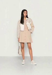 Jaqueta de ganga cinza claro, vestido beige sem mangas com detalhes em botão, sapatilhas bege e uma pequena mala clara. Design simples e cores suaves.