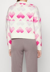 Strickpullover in Creme mit ombreförmigen rosa Herzmustern. Verfügt über einen runden Halsausschnitt und gerippte Bündchen. Cropped-Design mit lockerer Passform.