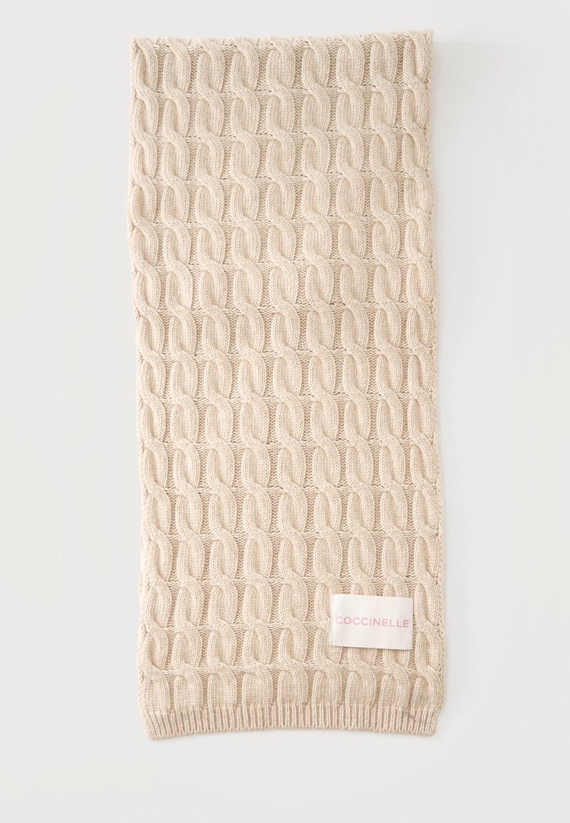 Écharpe beige tricotée avec un motif torsadé et une étiquette blanche rectangulaire portant la mention "COCCINELLE" en lettres rose clair.
