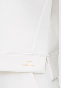 White sweatshirt with a textured finish, featuring a subtle gold "VENICE BEACH" logo near the hem and a unique folded design at the sleeves.
