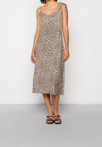 Robe midi à imprimé léopard avec fines bretelles, décolleté en V et tissu fluide. Associée à des sandales noires à lanières.