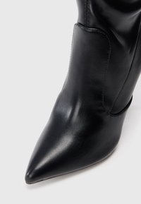 Fekete bőrszárú csizma hegyes orral és sima felülettel. Oldalsó varrással és diszkrét díszítéssel a széleken.