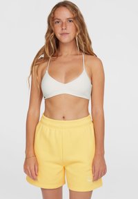 Bralette triangolare grigio chiaro con spalline sottili abbinato a pantaloni corti gialli con vita elastica, caratterizzati da una piccola grafica testuale all'orlo.