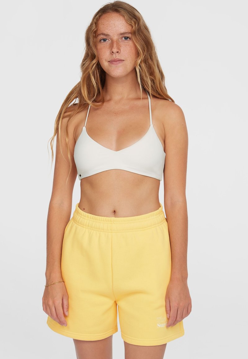 Bralette triangolare grigio chiaro con spalline sottili abbinato a pantaloni corti gialli con vita elastica, caratterizzati da una piccola grafica testuale all'orlo.