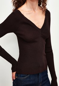 Haut marron à rayures, à manches longues, avec un décolleté en V. Présente des manches ajustées et une finition texturée, associé à un jean en denim bleu.