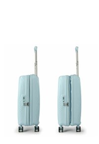 Valise rigide bleu clair avec un motif de vagues texturé, dotée de deux fermetures éclair, d'une poignée latérale et de quatre roues noires pour la mobilité.