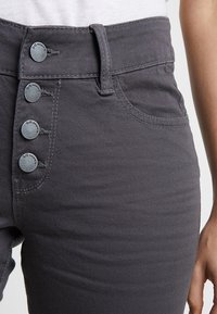 Jeans taille haute en denim gris avec cinq boutons décoratifs, poches avant et détails de couture subtils à la taille et à l'ourlet.