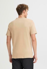 Beige cotton t-shirt with short sleeves, crew neck, and smooth texture, viewed from the back, paired with black shorts.