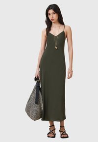 Vestido maxi verde oliva con tirantes finos, diseño elegante, textura suave. Combinado con un bolso a rayas en blanco y negro y sandalias negras.