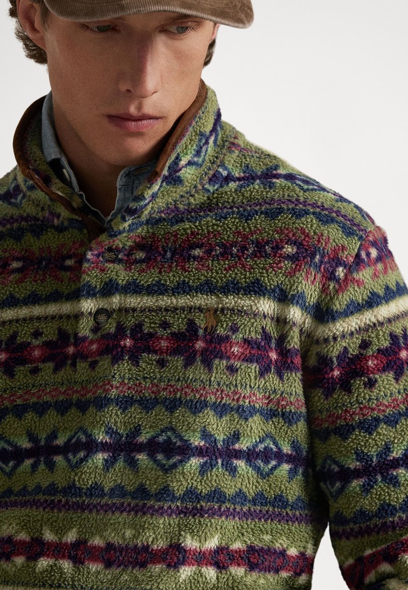 Polaire vert avec motifs géométriques multicolores en violet, bleu et rouge. Doté d'un col marron et de détails à boutons.