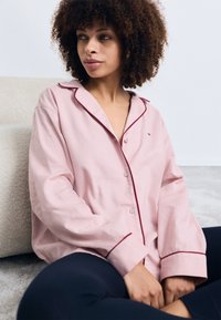 Rosa skjorta med knapp-up och röd piping samt långa ärmar. Mjuk tyg med en avslappnad passform. En liten logotyp är synlig på bröstet.