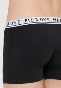 Czarne bawełniane bokserki z białą elastyczną gumą w pasie, na której znajduje się napis "PIER ONE" w czarnym kolorze. Gładka tekstura i dopasowany krój.