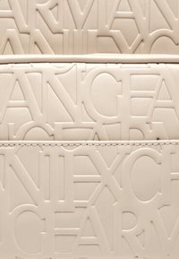 Borsa beige texturizzata con lettere in rilievo, design strutturato, superficie liscia e cuciture a contrasto lungo le cuciture.