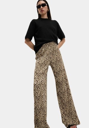 Leopard print wide-leg pants in beige and black; paired with a black loose-fitting top. Model wearing sunglasses and gold hoop earrings.