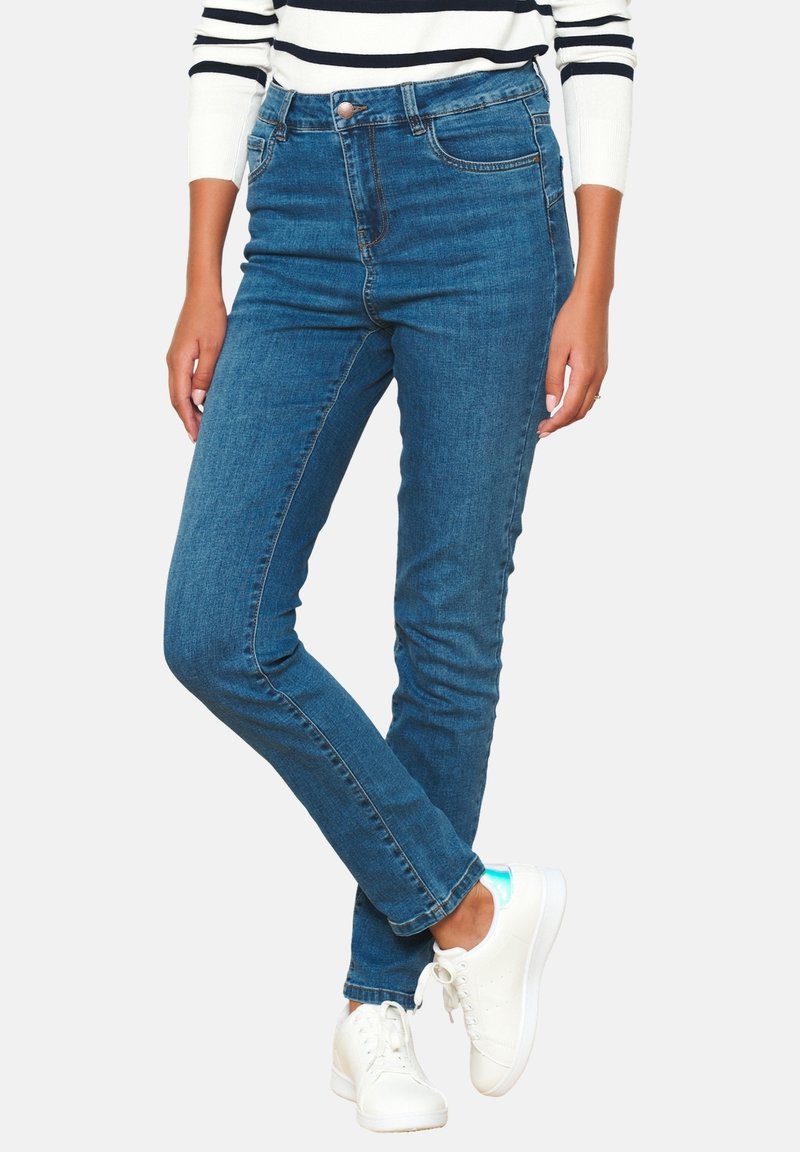 Tievā piegriezuma zili džinsi ar vidēju vidukli un maigu izbalējumu. Saskaņoti ar baltām sporta apaviem, kuriem ir vienkārši akcenti un gluda tekstūra.