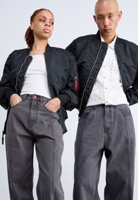 Des vestes bombardier noires avec un design perforé, associées à un pantalon taille haute gris avec des coutures contrastantes. Ajustement slim, matériaux texturés.